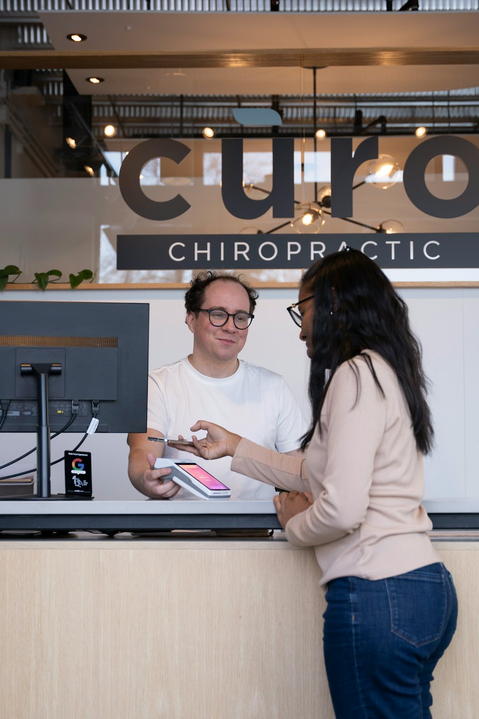 Employee holds payment terminal for customer tapping phone at reception desk.